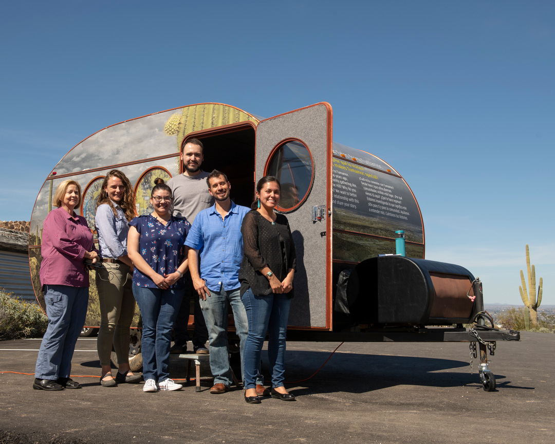 Researchers stand in front of a camper painted with desert scenes